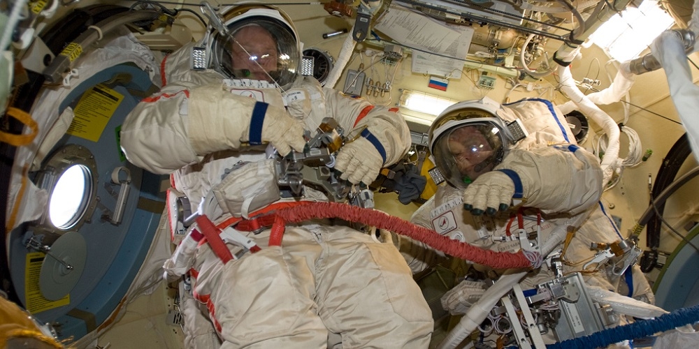 Twee ruimtevaarders maken zich klaar om een ruimtewandeling uit te voeren vanuit de Russische Poisk module. 
