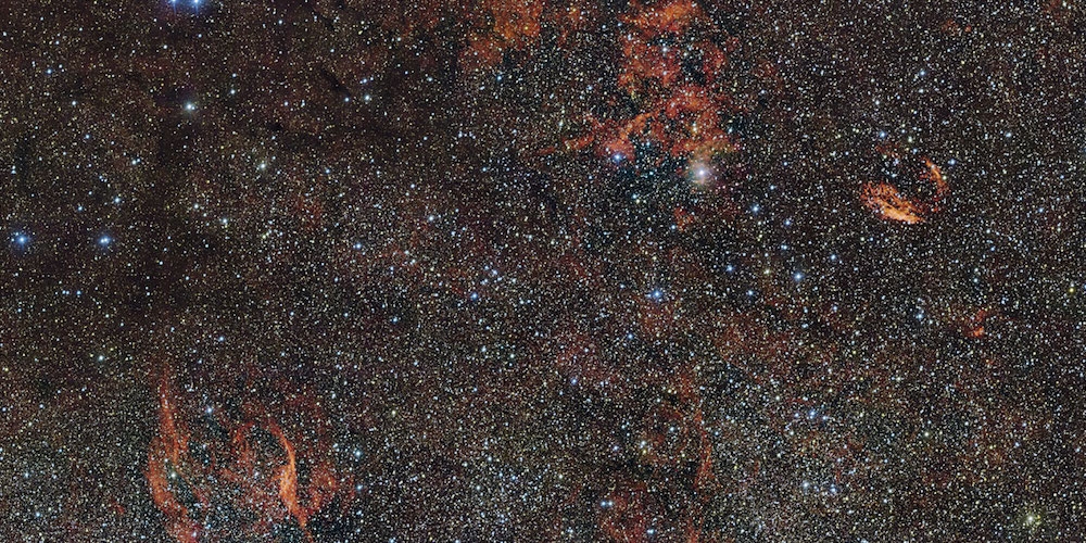 Op deze enorme foto van het zuidelijke sterrenbeeld Norma (Winkelhaak) zijn slierten van karmozijnrood gas te zien, die worden verlicht door zeldzame, zware sterren die pas recent zijn ‘ontbrand’ en nog diep verscholen zitten in dikke stofwolken